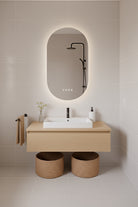 Modern bathroom with wooden vanity, pill shaped LED mirror, and decorative elements.
